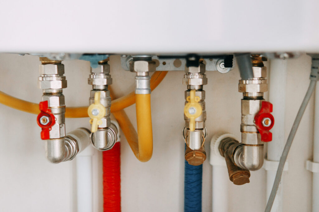 Close-up view of water heater pipes and valves in a utility room, featuring colorful connectors and tubes. Essential components for heating system maintenance and operation. Gas boiler taps.